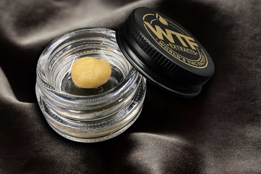 Close-up of golden live rosin concentrate in a small glass jar on a natural wood surface.